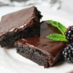 two layered slices of hershey frosted brownies garnished with mint leaves and fresh blackberries.