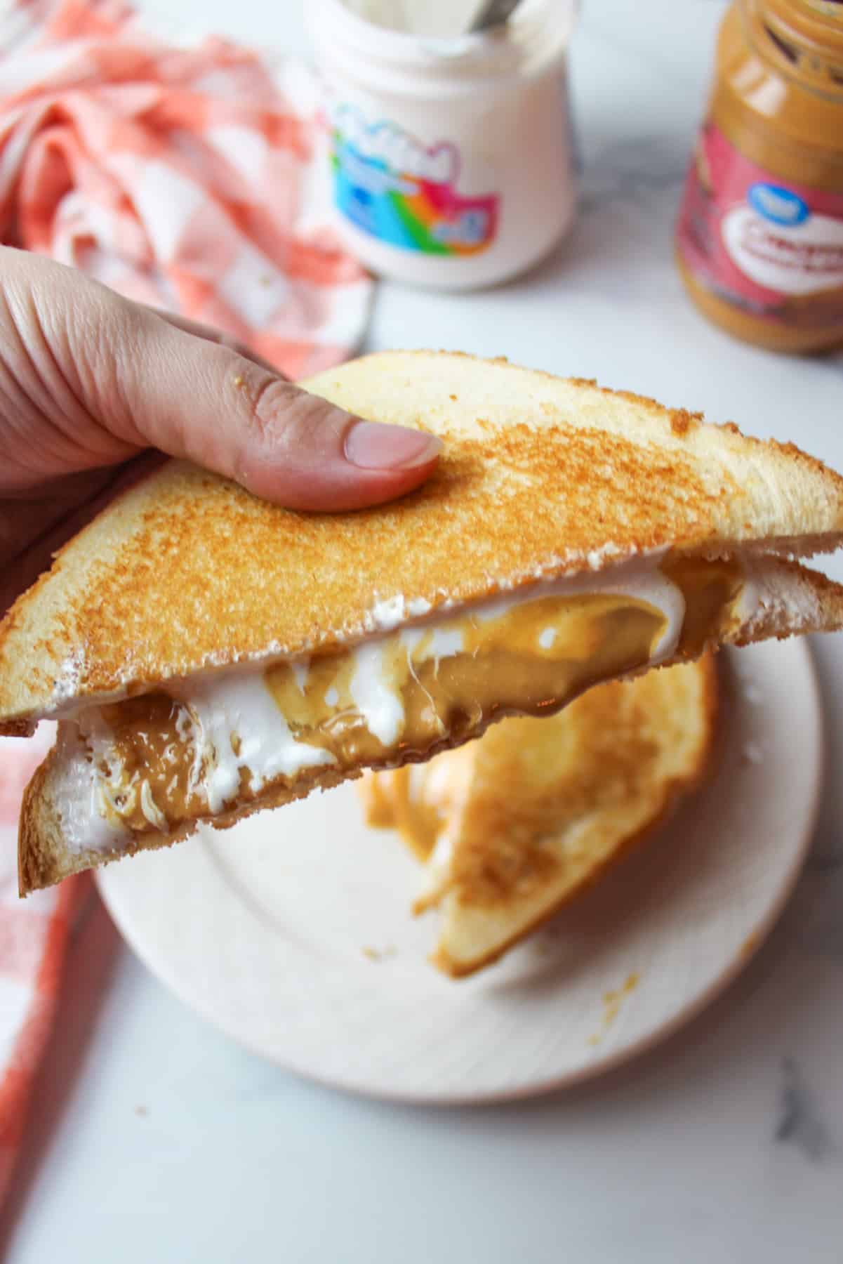 a hand holding a slice of grilled fluffernutter sandwich above a plate.