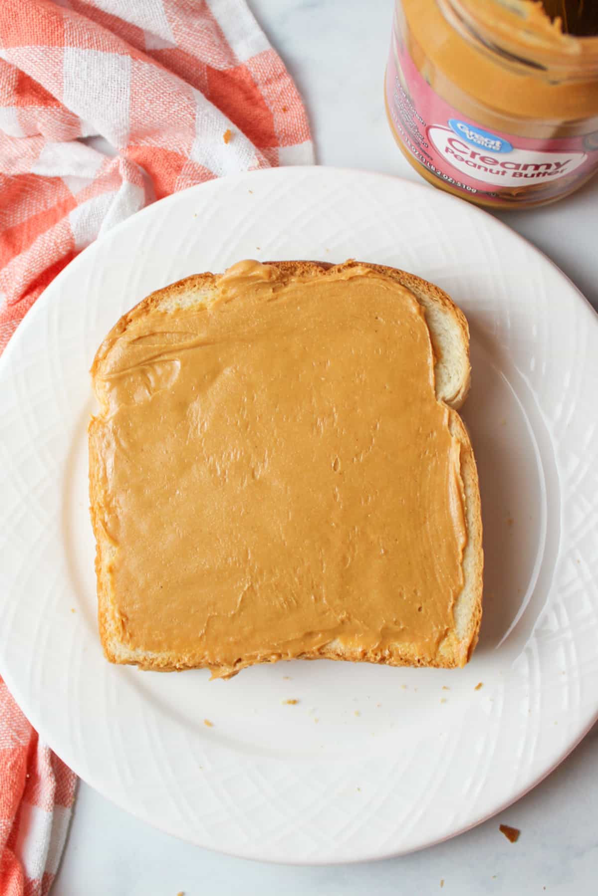 peanut butter spread onto a slice of bread on a white plate.