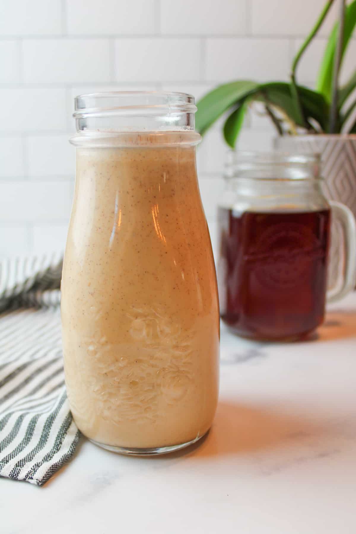 bottle of pumpkin creamer with a mug of coffee in the background.