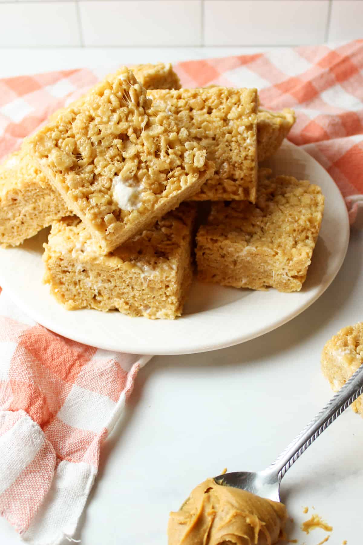 peanut butter rice krispie treats on a plate with a spoon of peanut butter in front