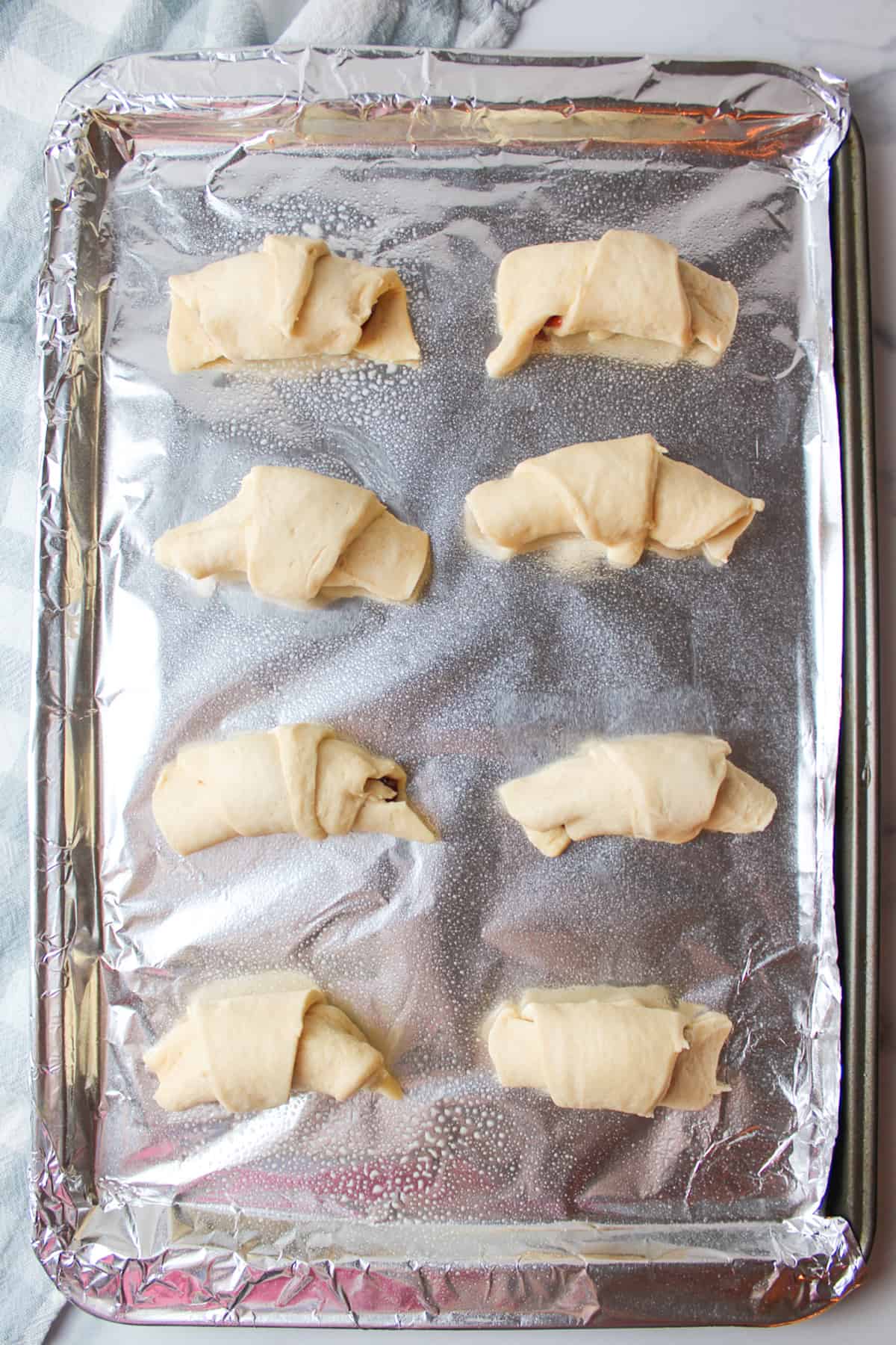 filled unbaked crescent rolls on a foil lined baking sheet