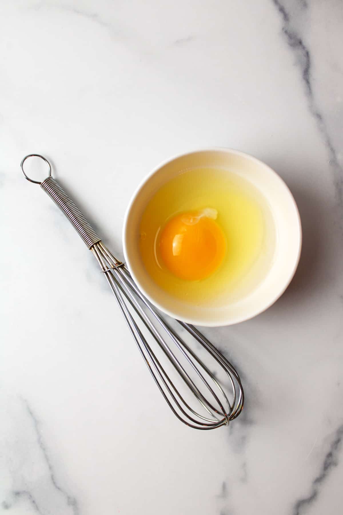 water and egg in a bowl with a whisk to the side.