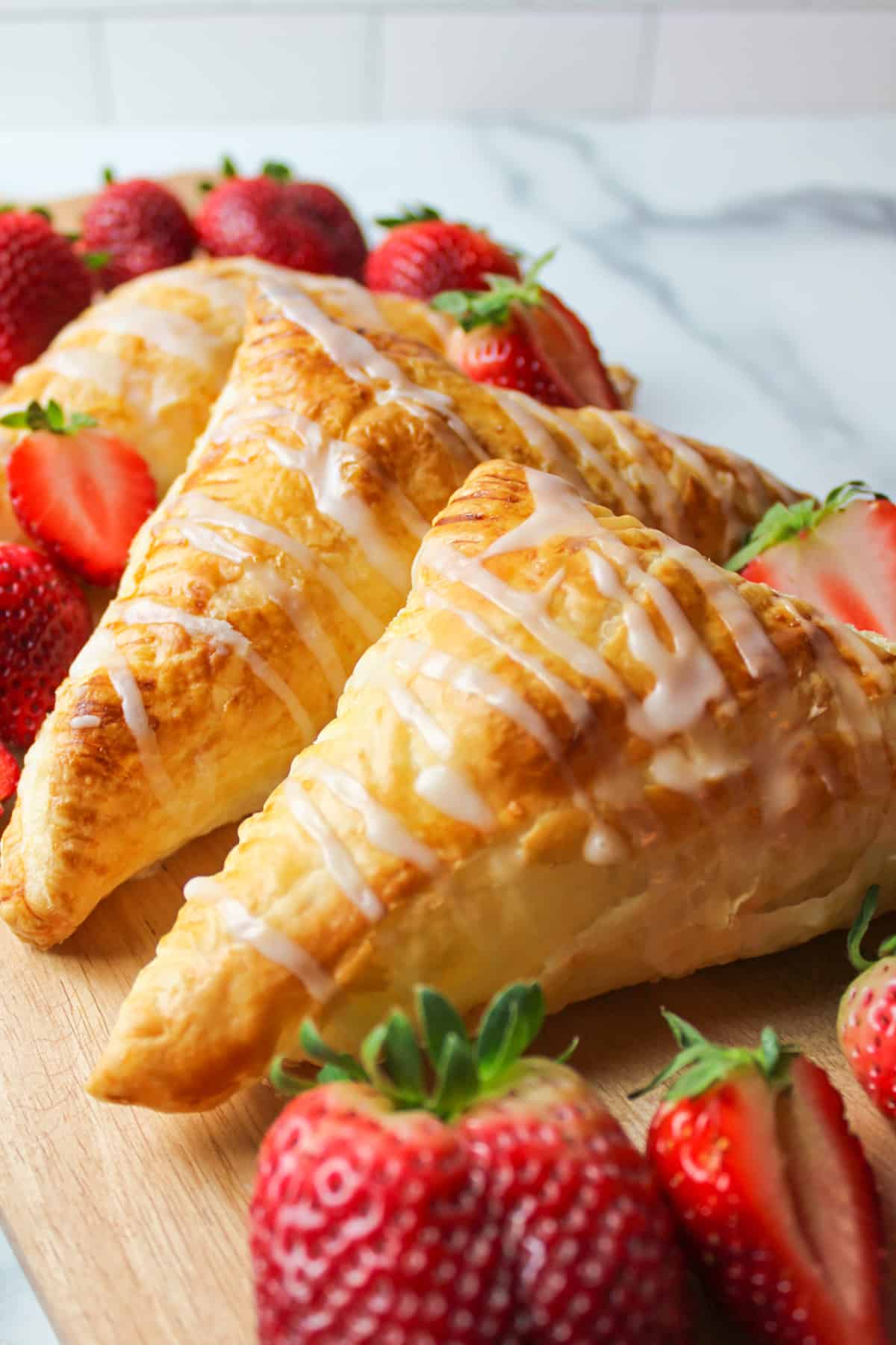 iced turnovers on a wooden board with fresh strawberries.