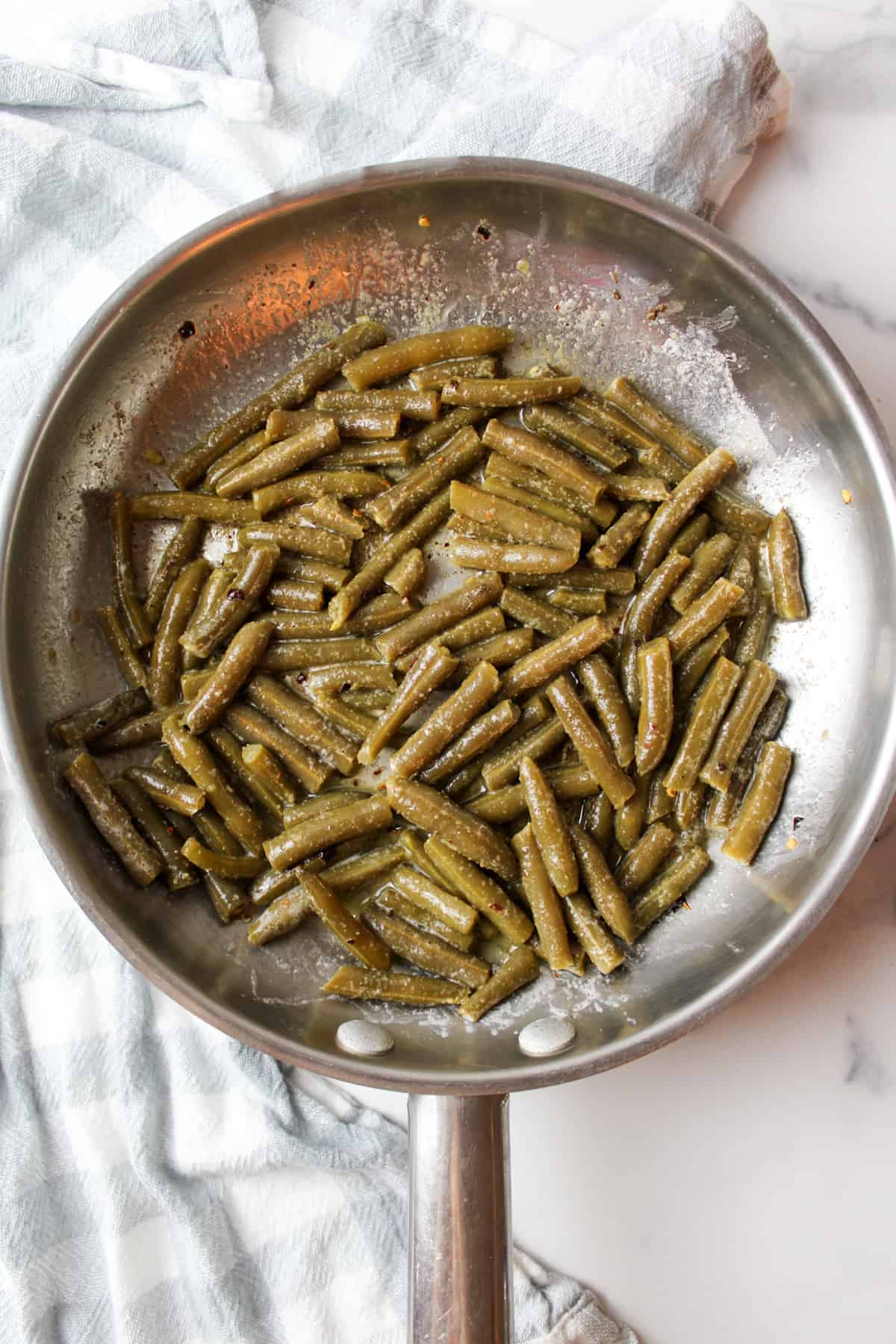 cooked canned green beans in a skillet mixed with seasonings.