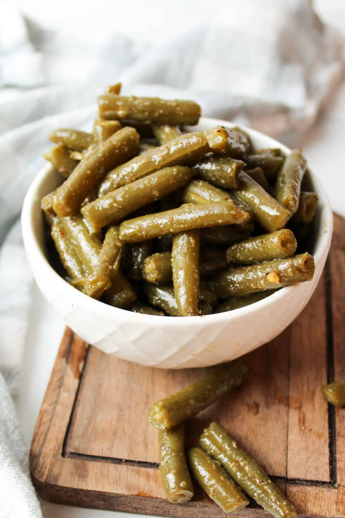 a bowl filled with cooked canned green beans with a few green beans below it.