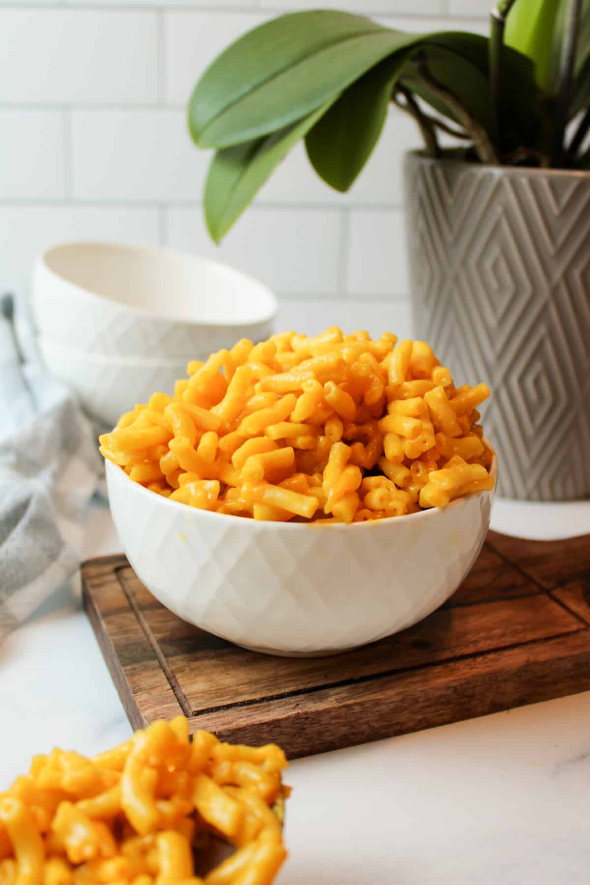 a heaping bowl of mac and cheese in front of a plant and empty bowls.