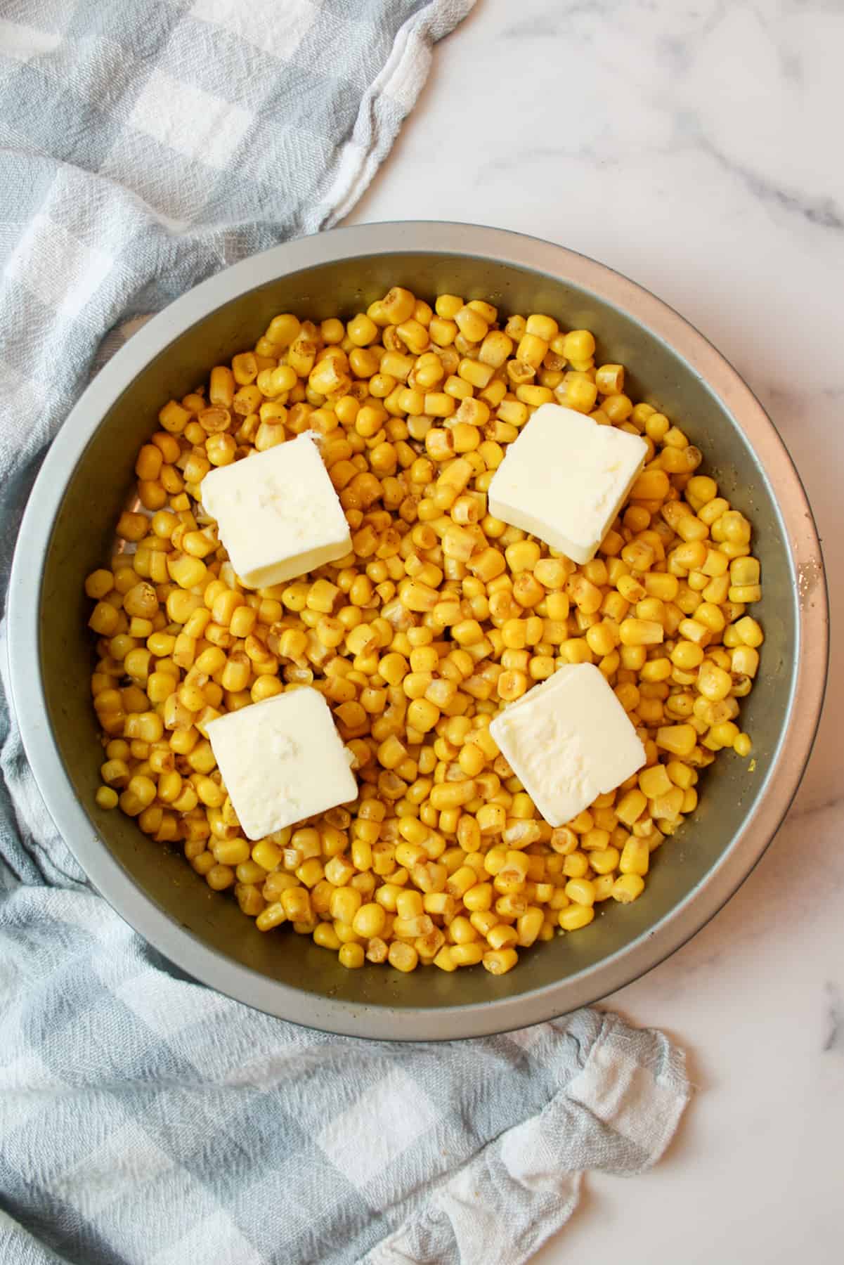 seasoned corn topped with 4 pads of butter in a cake pan