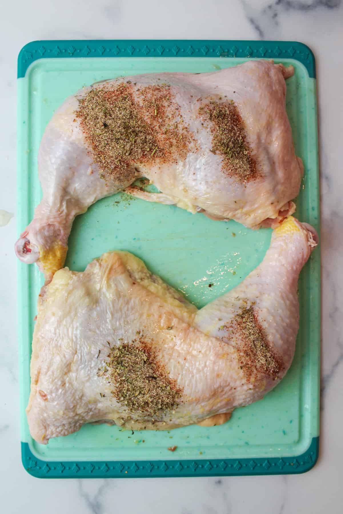 sprinkled seasoning over chicken quarters on cutting board.
