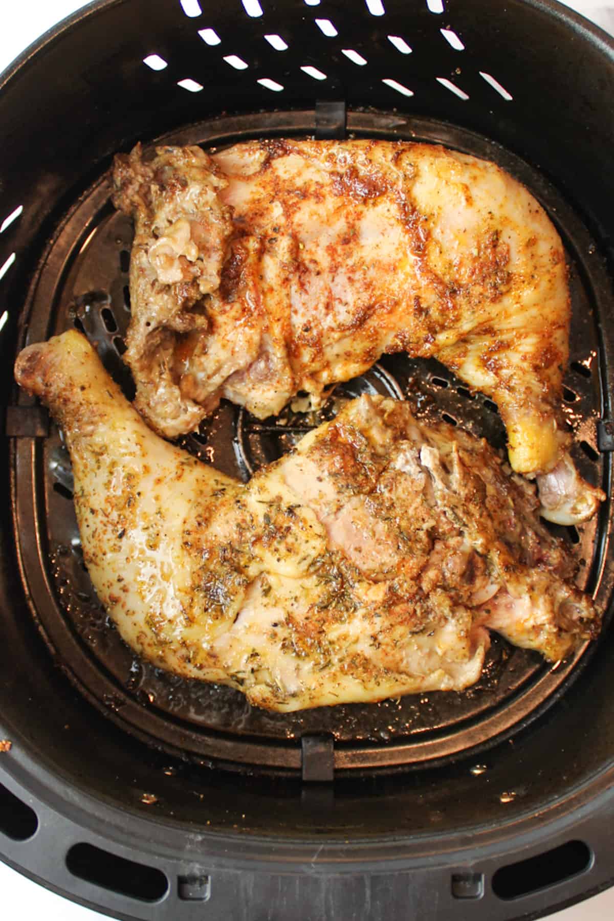 two chicken quarters in an air fryer basket flipped over to reveal the bottom side.
