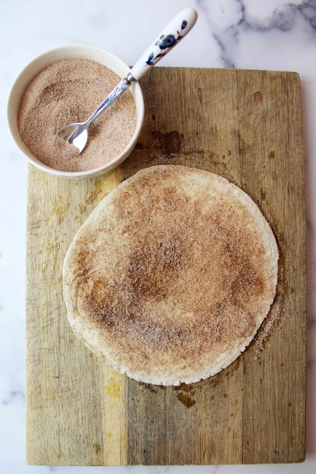 cinnamon sugar rubbed over tortilla with a bowl of cinnamon sugar and a spoon to the side.