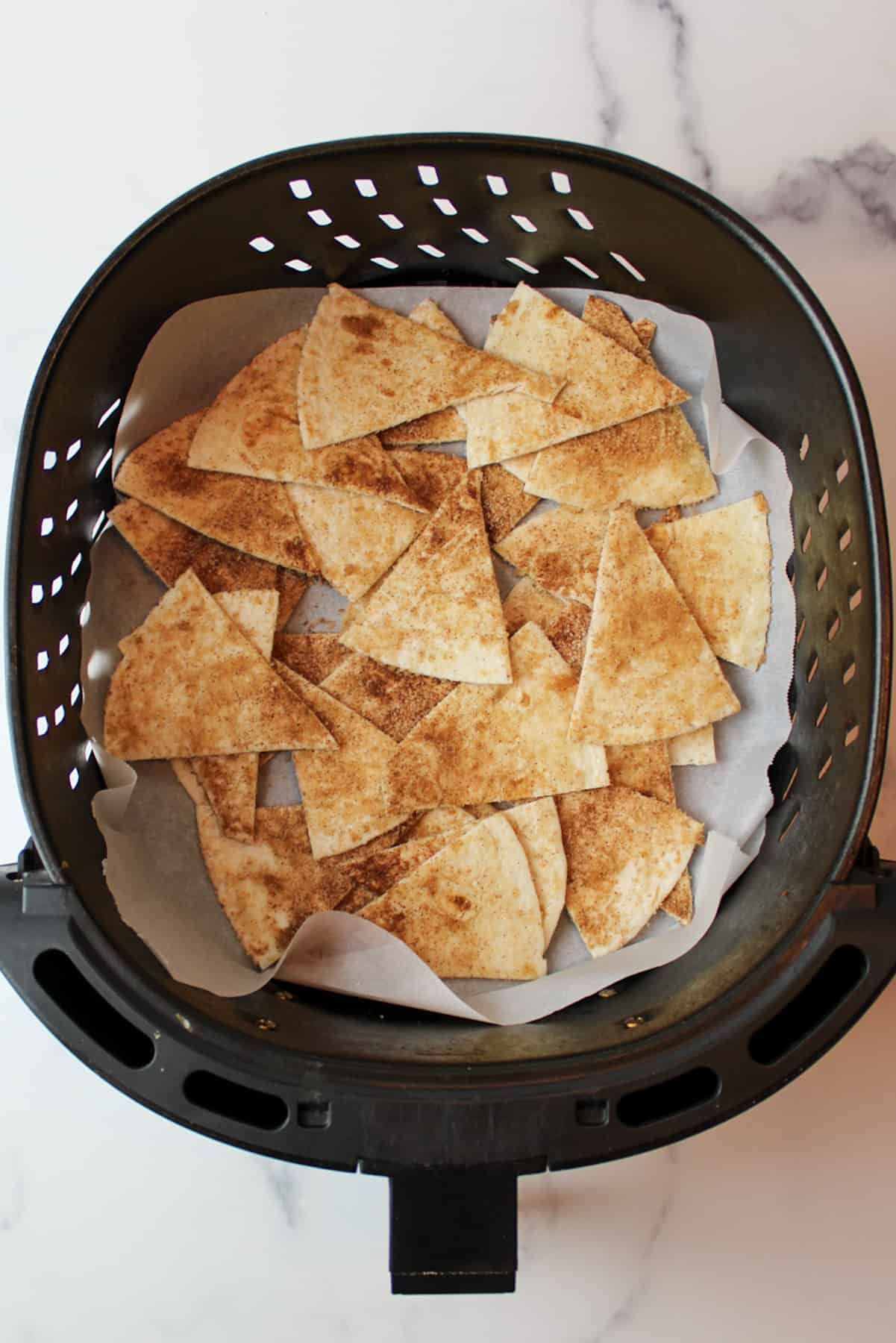 cinnamon sugar tortilla chips in an air fryer basket lined with parchment paper