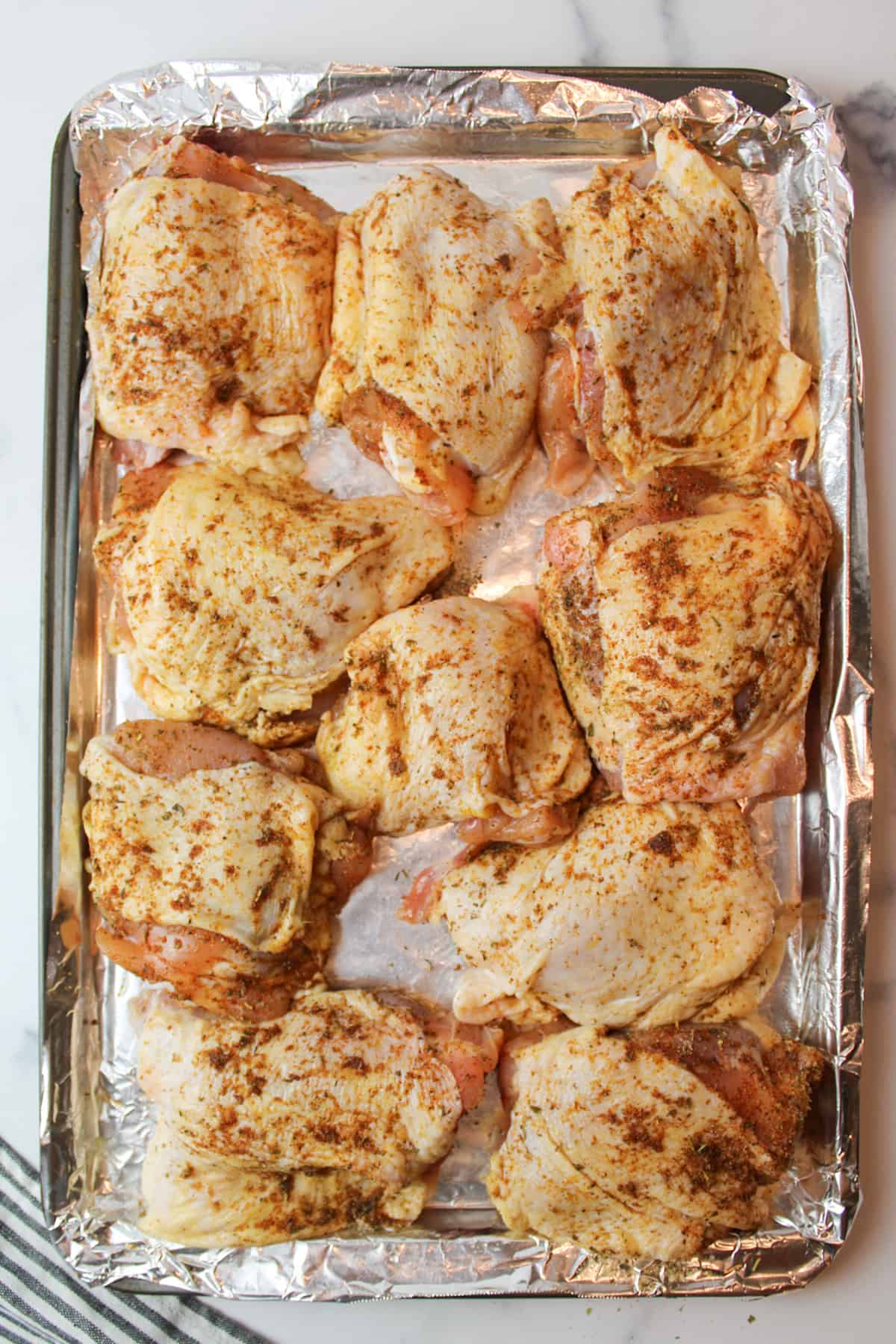 seasoning covered chicken thighs on a foil lined baking sheet