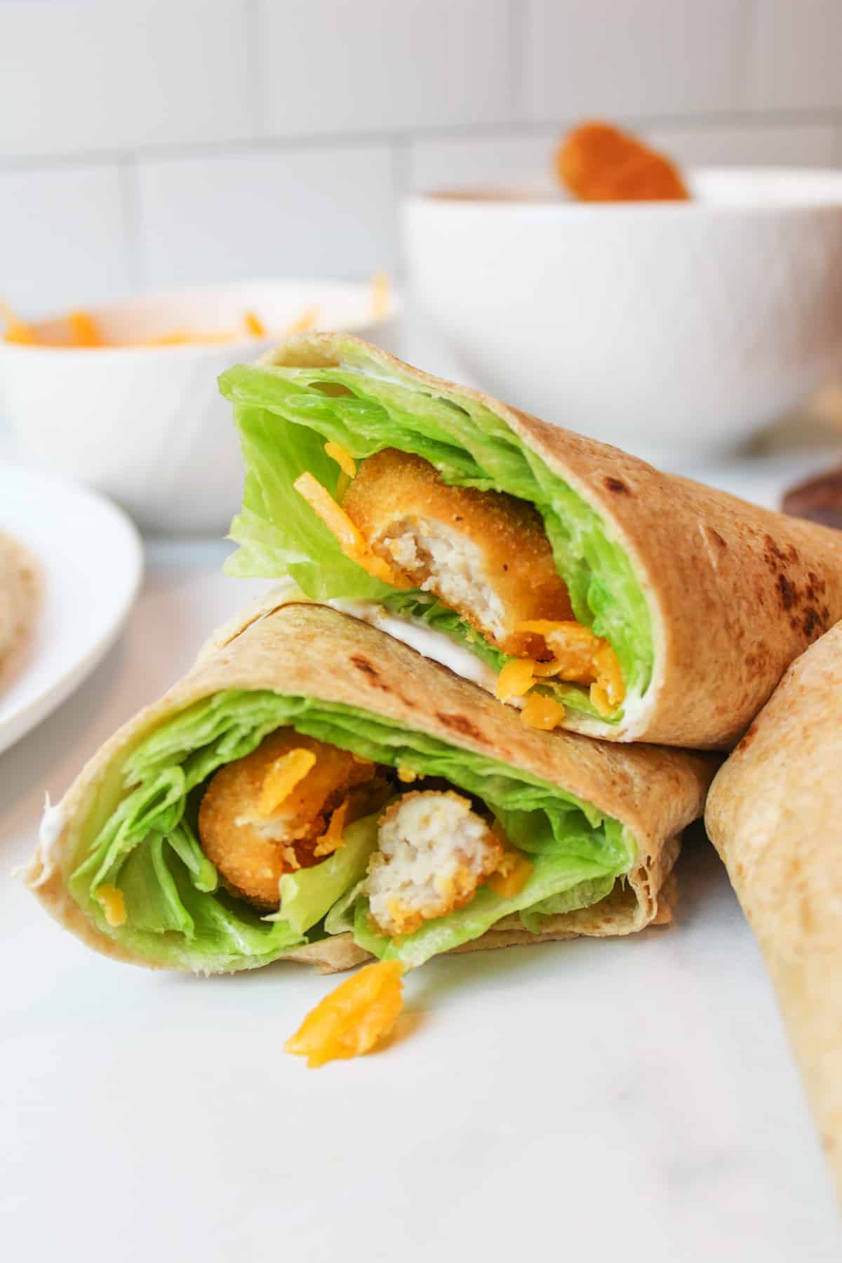 chicken nugget wraps stacked on eachother with bowls of ingredients in the background.