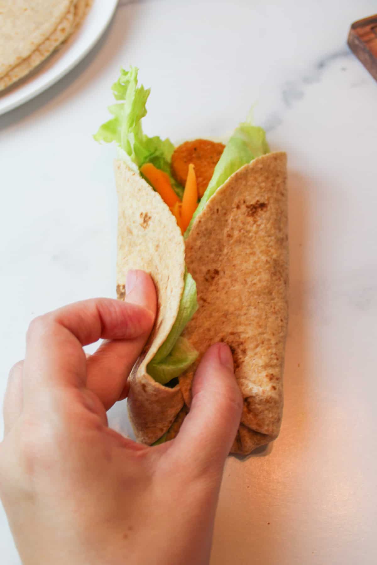 a hand pinching the sides of the chicken nugget wrap together.