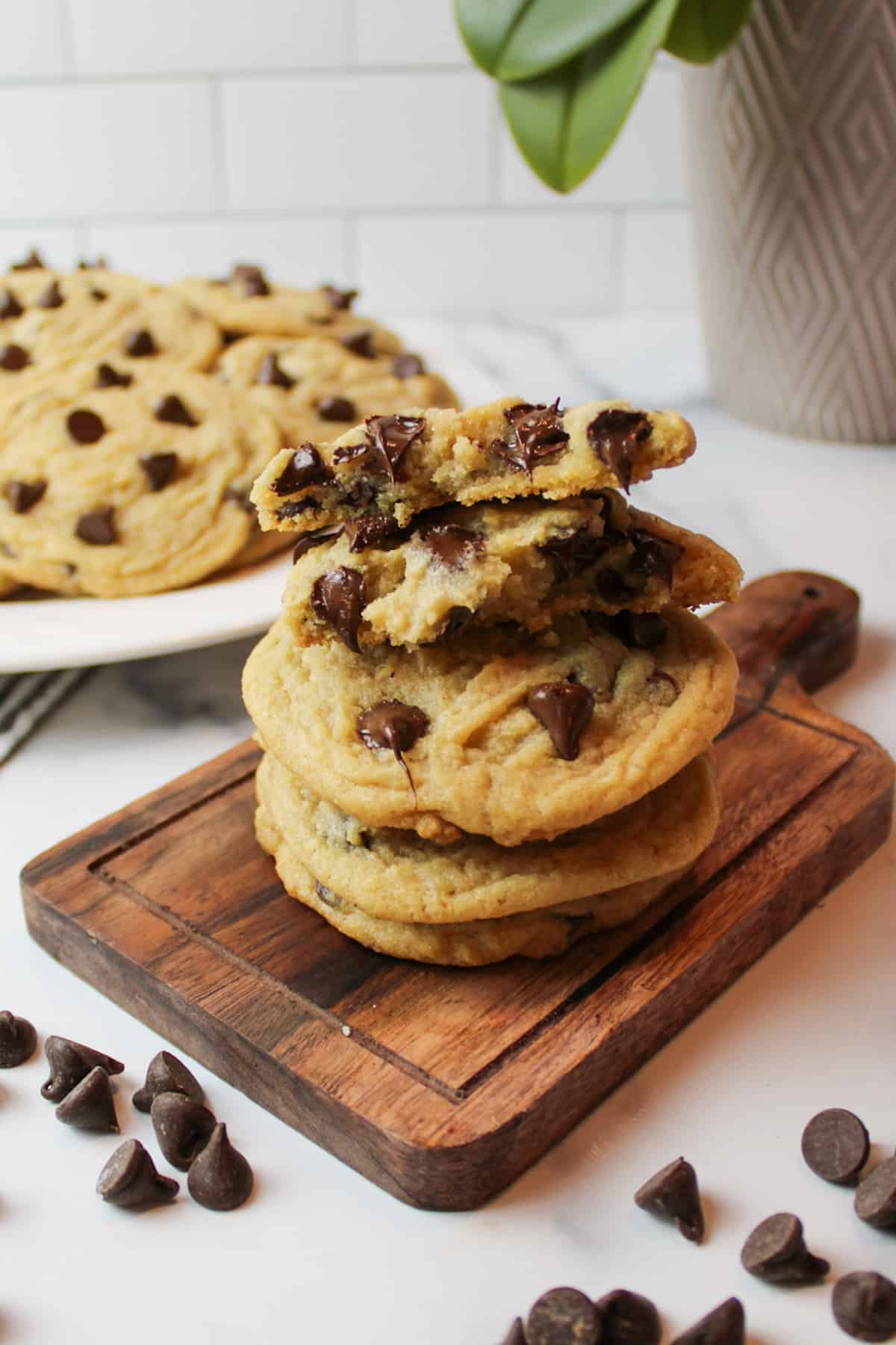 stacked chocolate chip cookies on a wooden boad with the top cookie broken in half