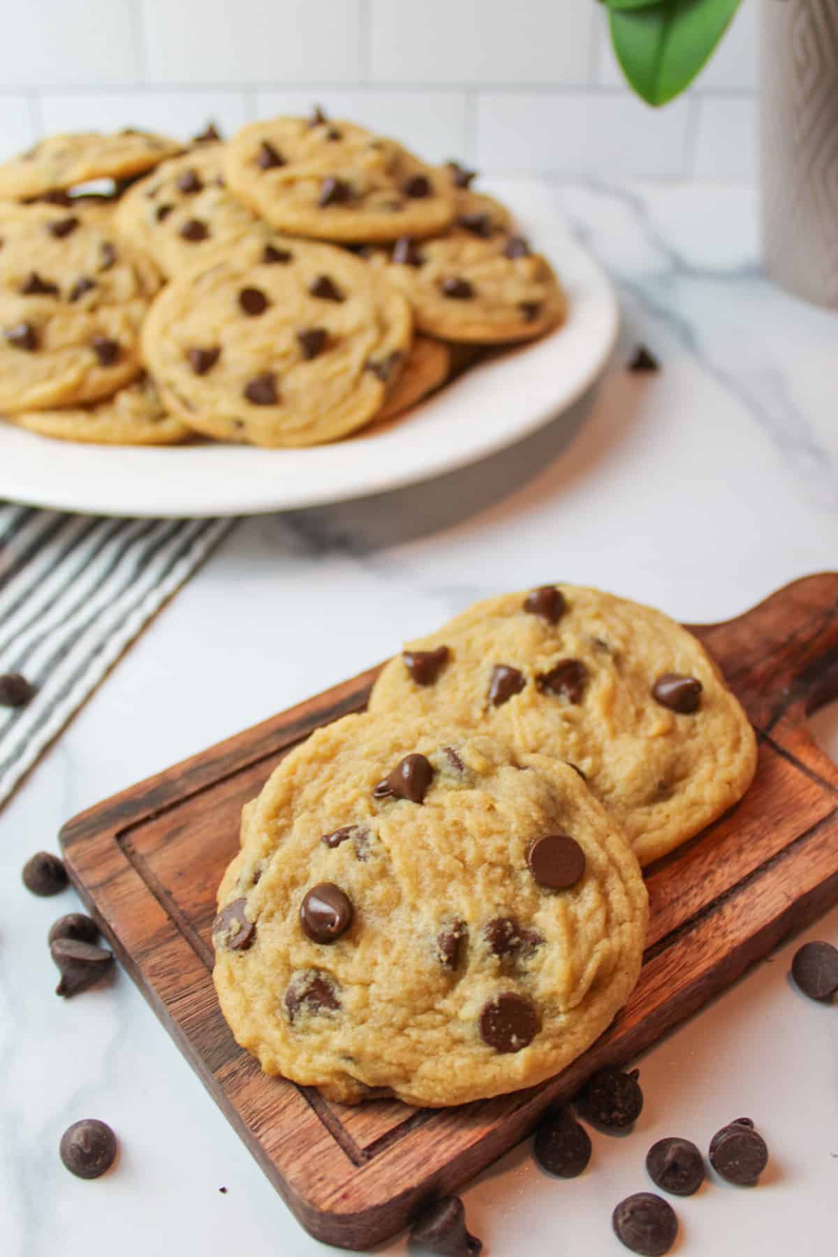 chocolate chip cookies on a small cutting board and on a plate in the background.