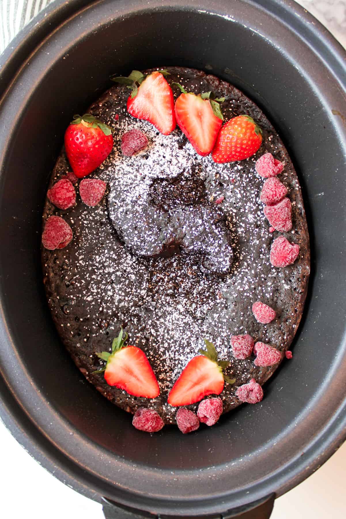 chocolate lava cake in a crockpot with powdered sugar and red berries on top.
