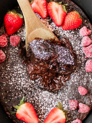 an upclose view of chocolate lava cake in a crockpot with powdered sugar a wooden spoon and red berries