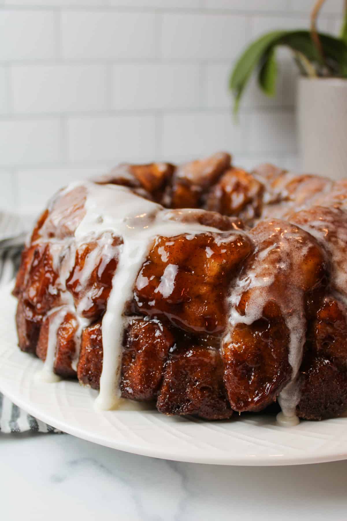 Cinnamon roll monkey bread on white plate with dripping icing.