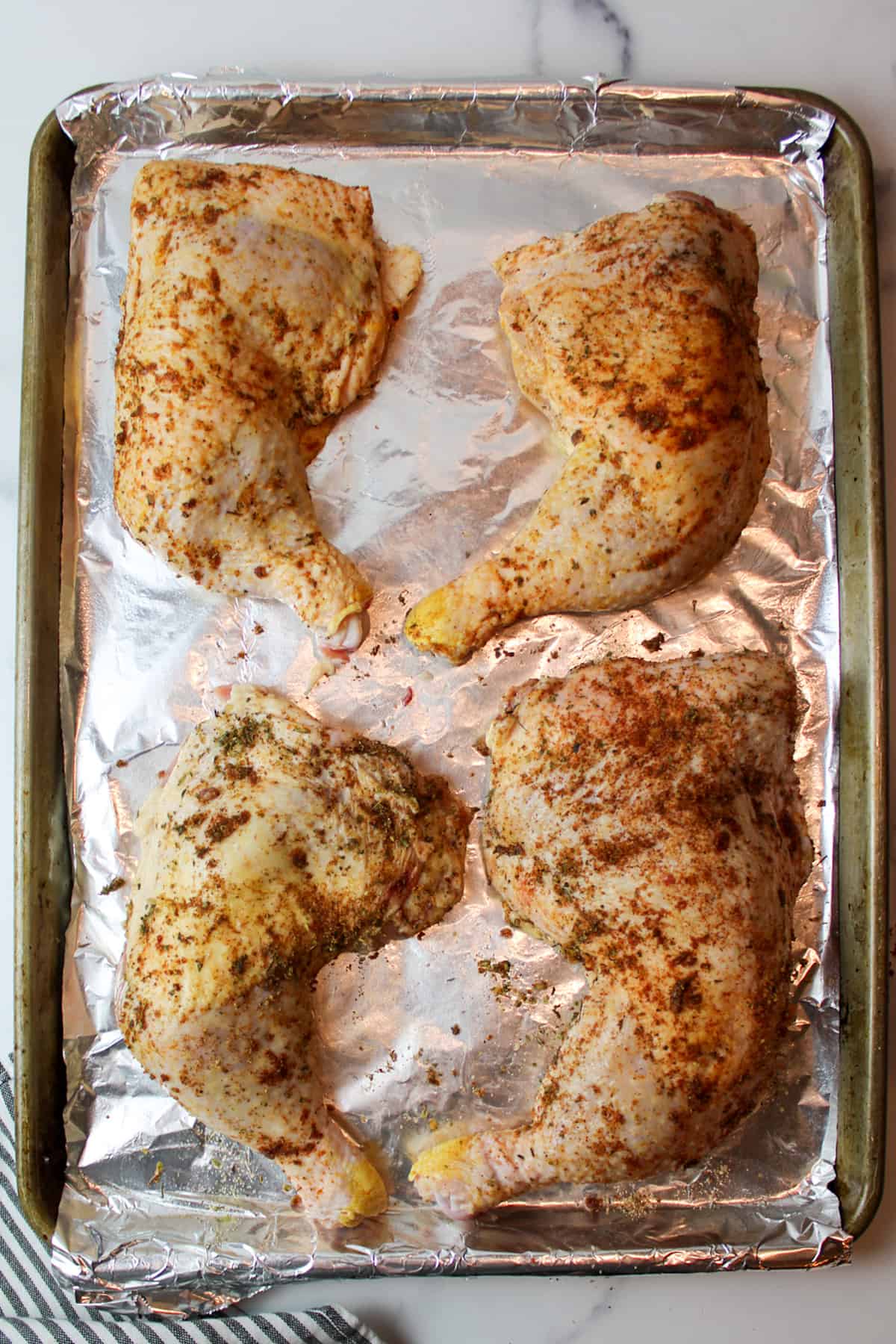 seasoning coated raw chicken quarters on a foil lined baking sheet.