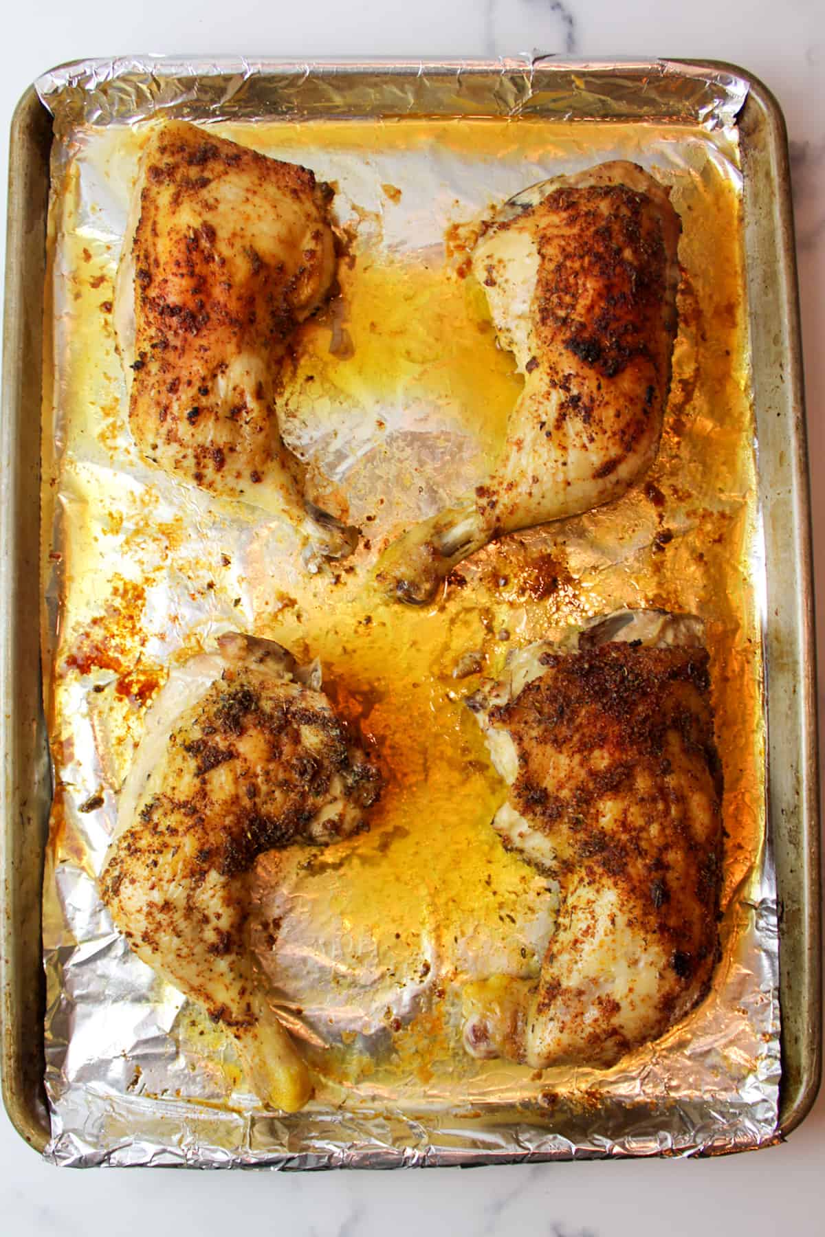 baked seasoned chicken quarters on a foil lined baking sheet.
