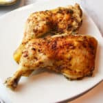 two crispy chicken quarters on a square plate.