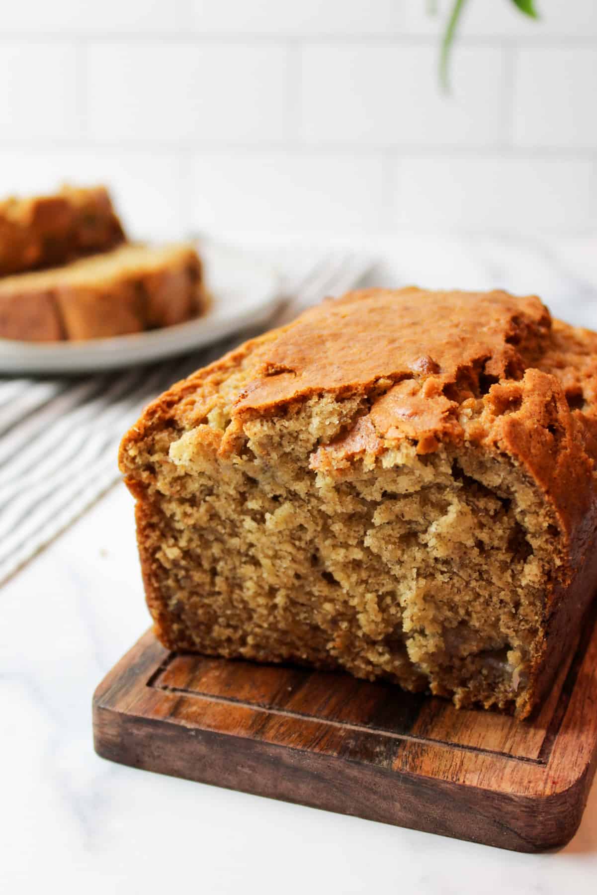 eggless banana bread on a wooden cutting baord with more sliced on a plate in the background
