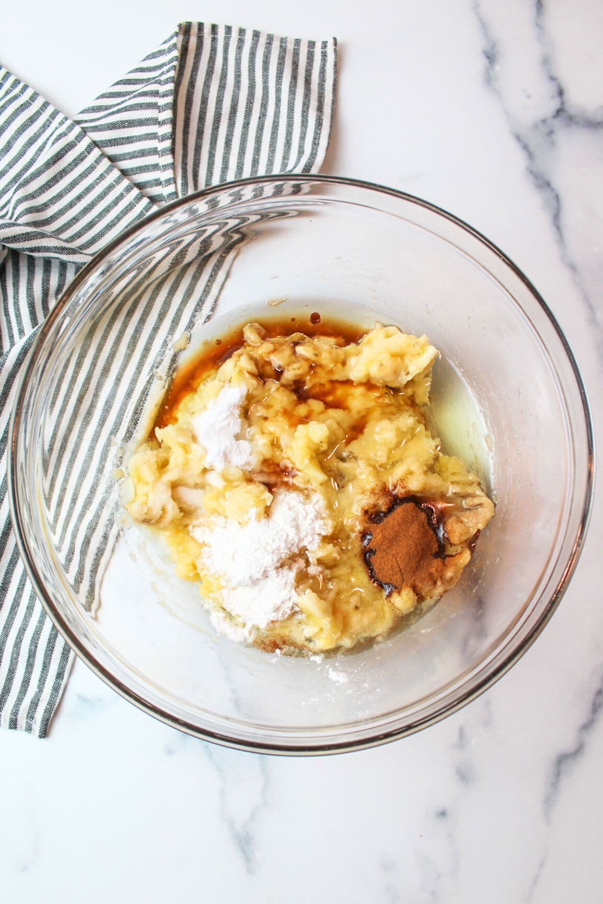 cinnamon oil and leavening agents added to mashed banana in a bowl.