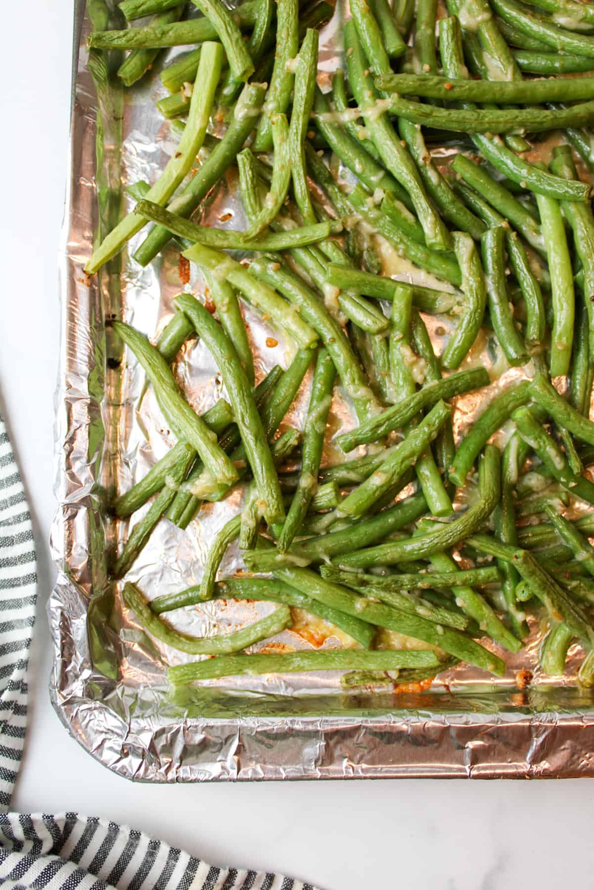 aerial view of a corner of a baking sheet topped with foil and roasted parmesan garlic green beans