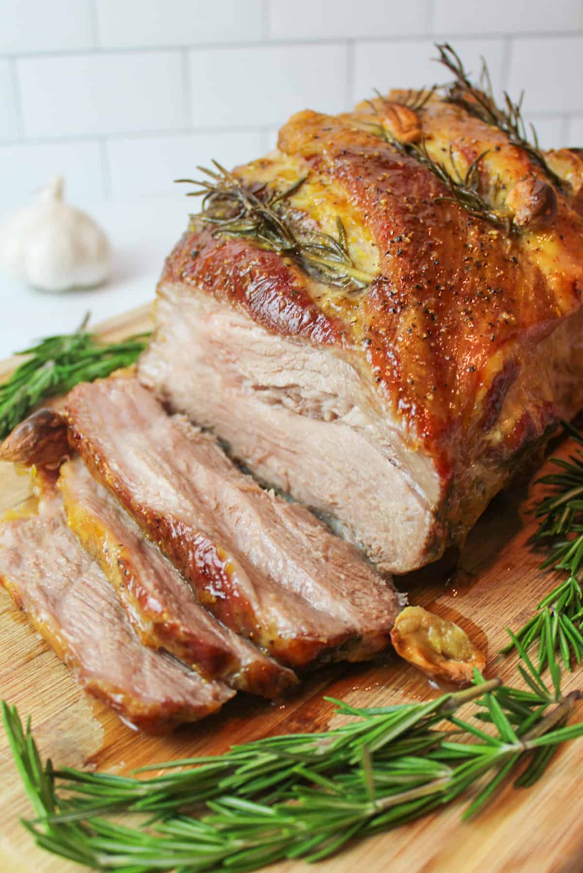 Sliced pork roast garnished with fresh rosemary and roasted garlic cloves on a cutting board.