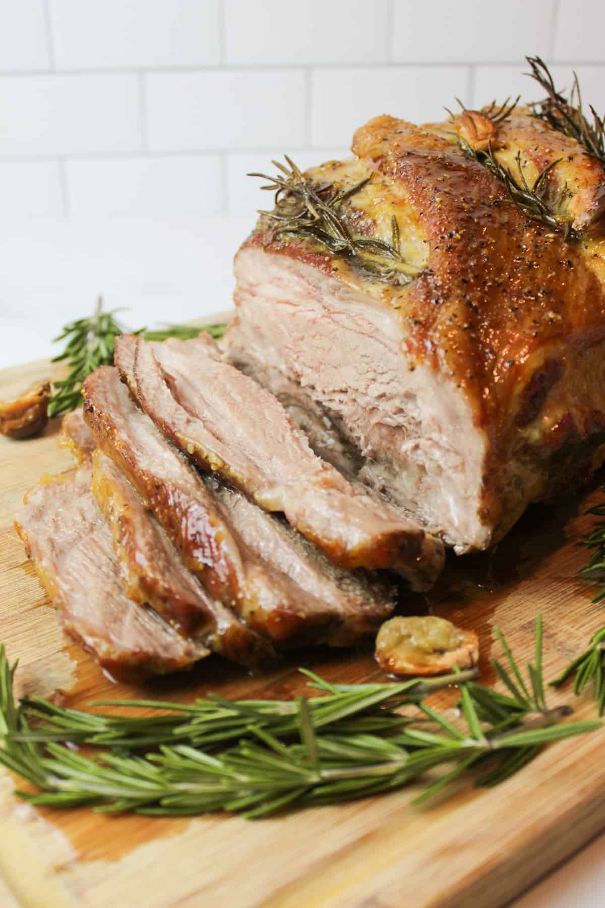 a sliced pork roast topped with rosemary and roasted garlic cloves.