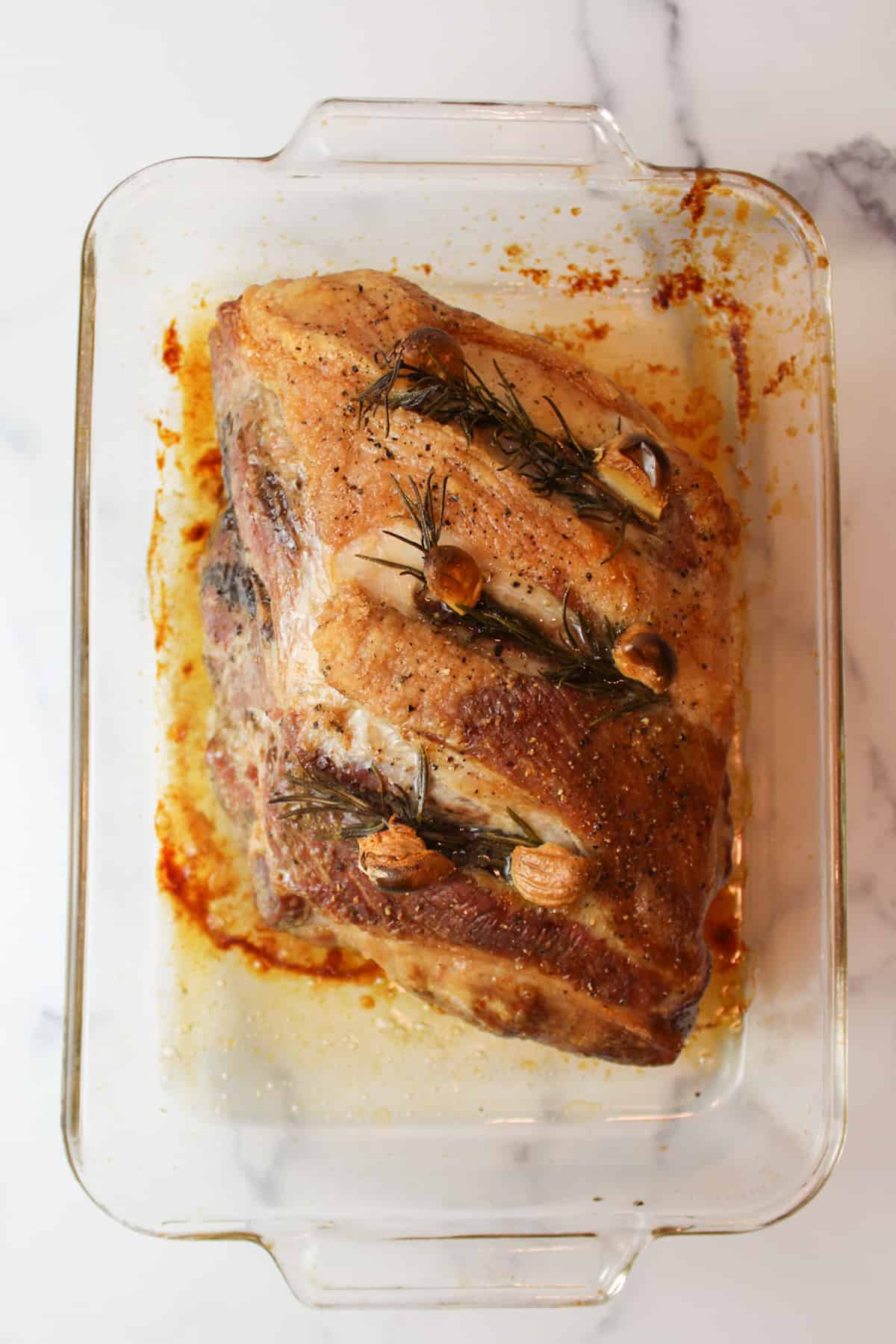 roasted pork shoulder with rosemary and garlic cloves in a glass 9x13 baking dish