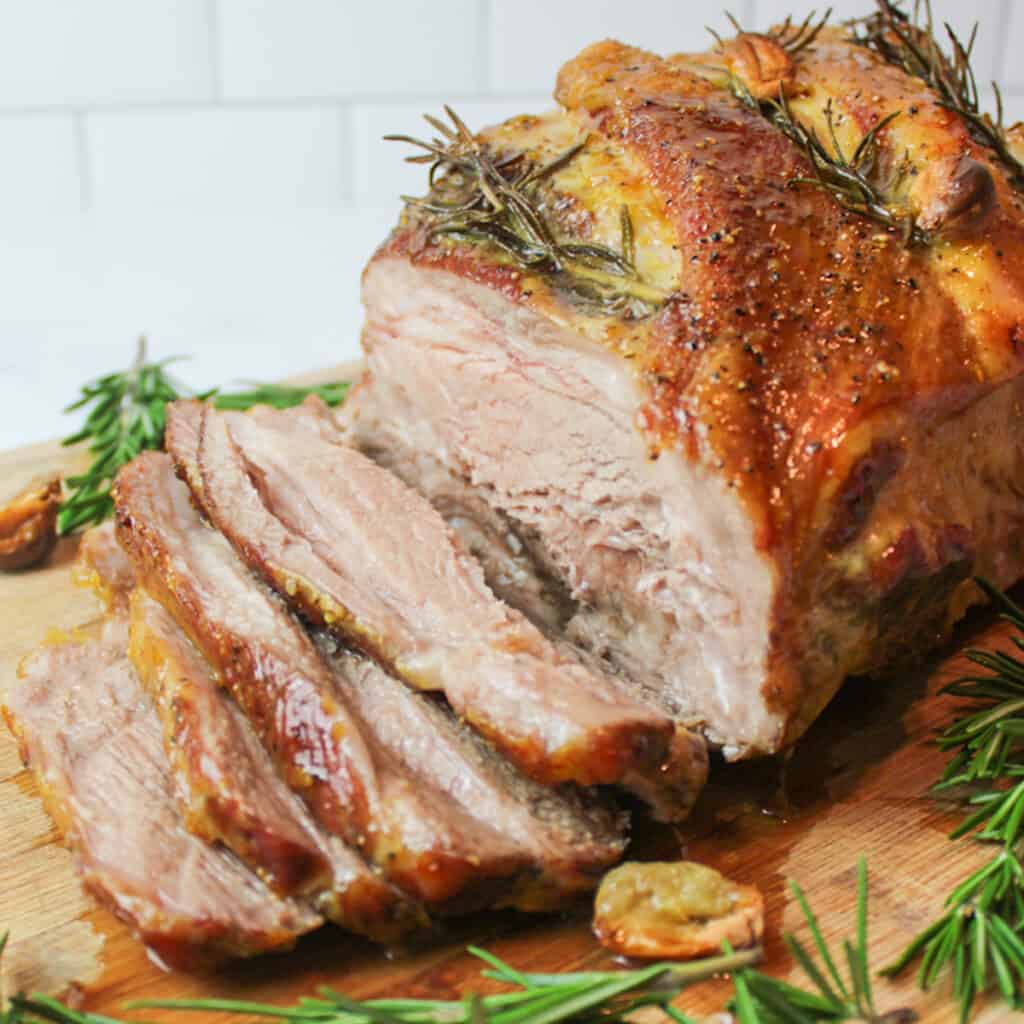 a sliced honey mustard pork shoulder roast with rosemary and garlic cloves.