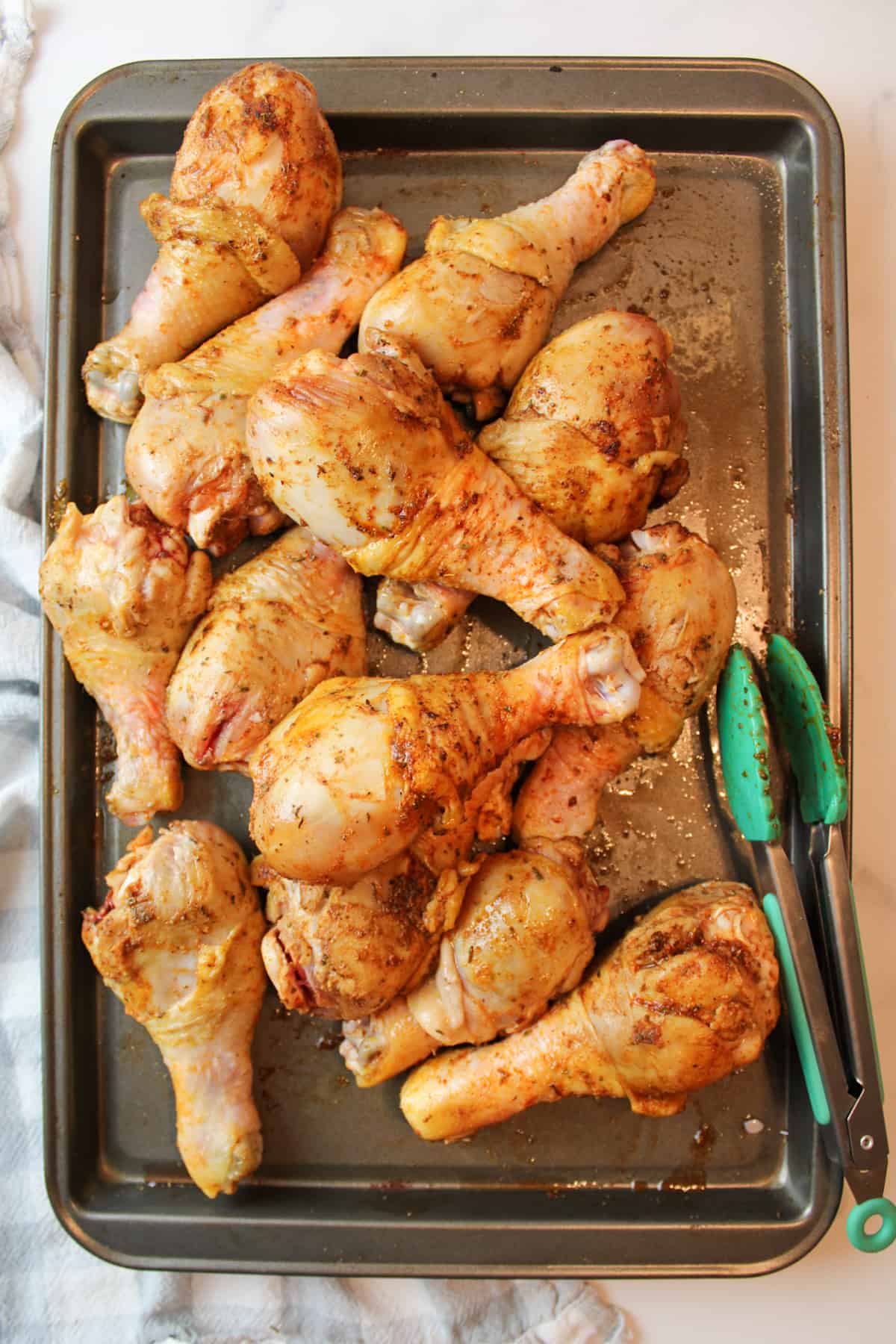 browned chicken legs on a baking sheet with a pair of tongs.