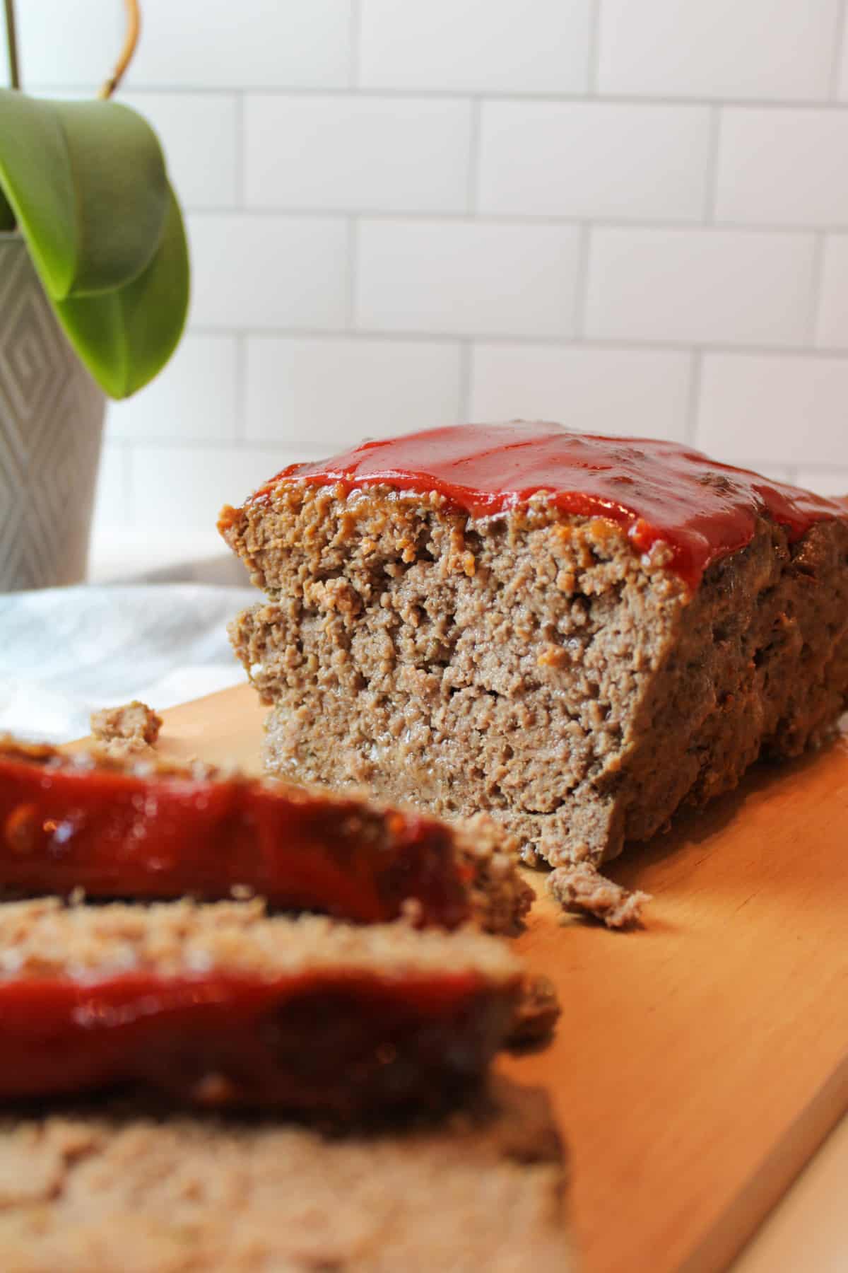 sliced meatloaf on a wooden cutting board with slices in front out of focus and meatloaf in background in focus
