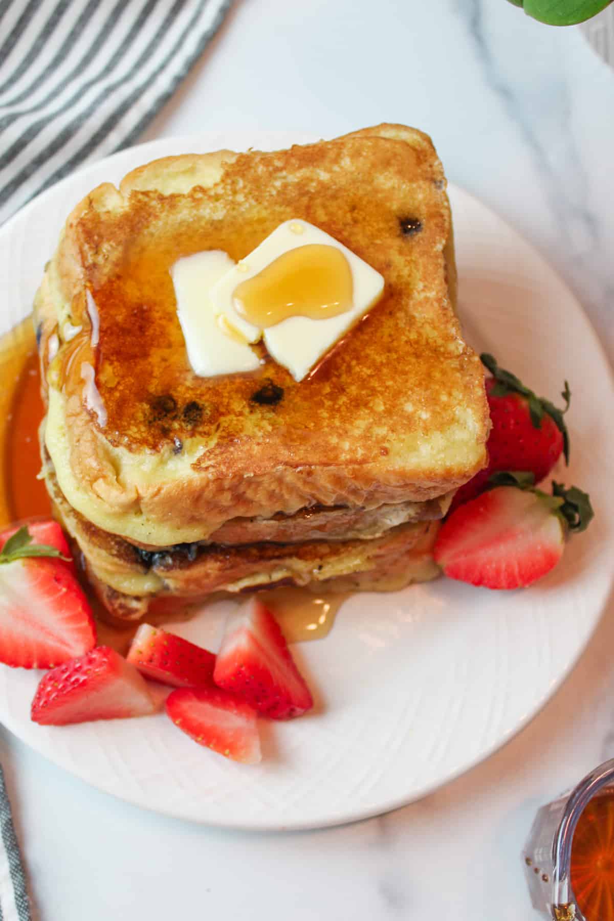 syrup and butter topped muffin mix french toast with fresh sliced strawberies to the sides