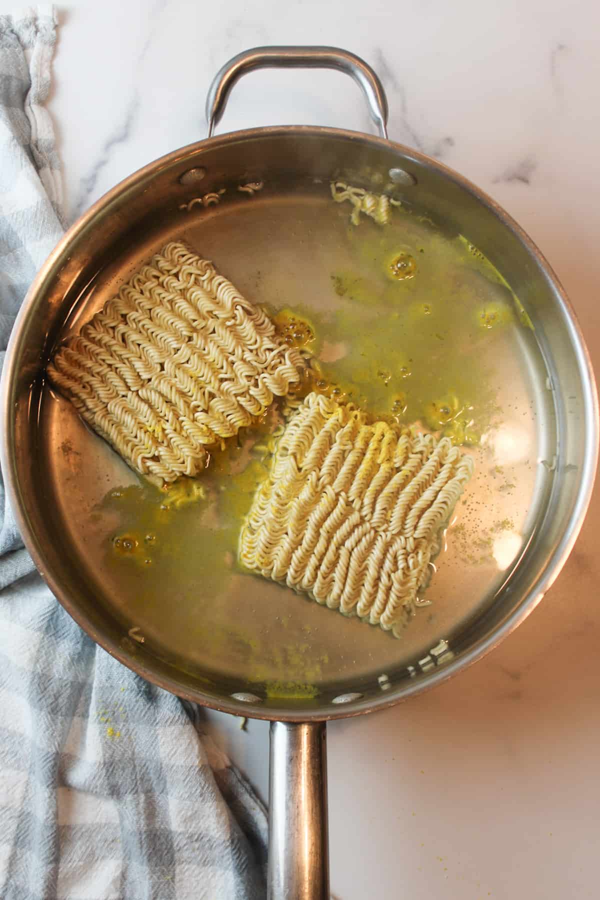 two ramen noodle squares in a large pan with some chicken seasoning and water