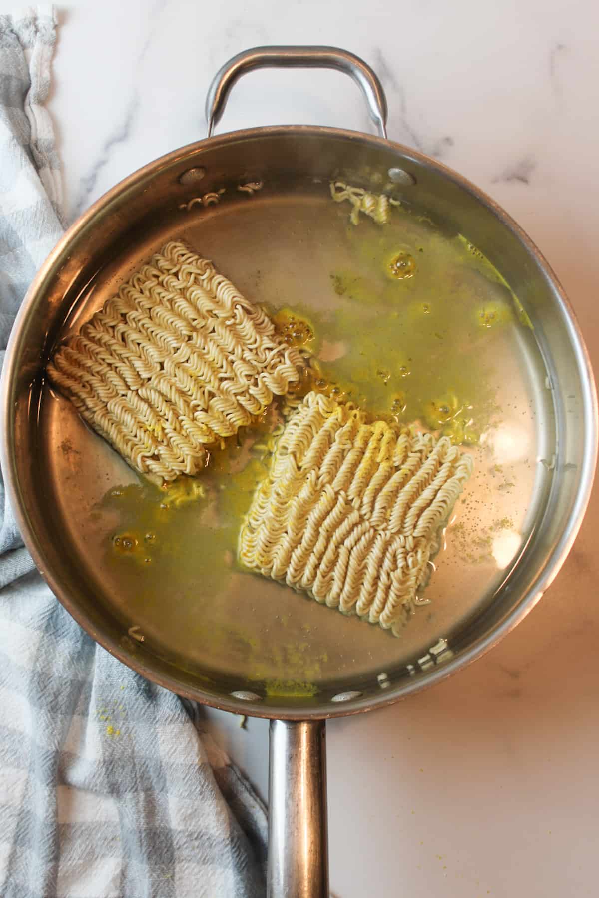 two ramen noodle squares in a large pan with some chicken seasoning and water.