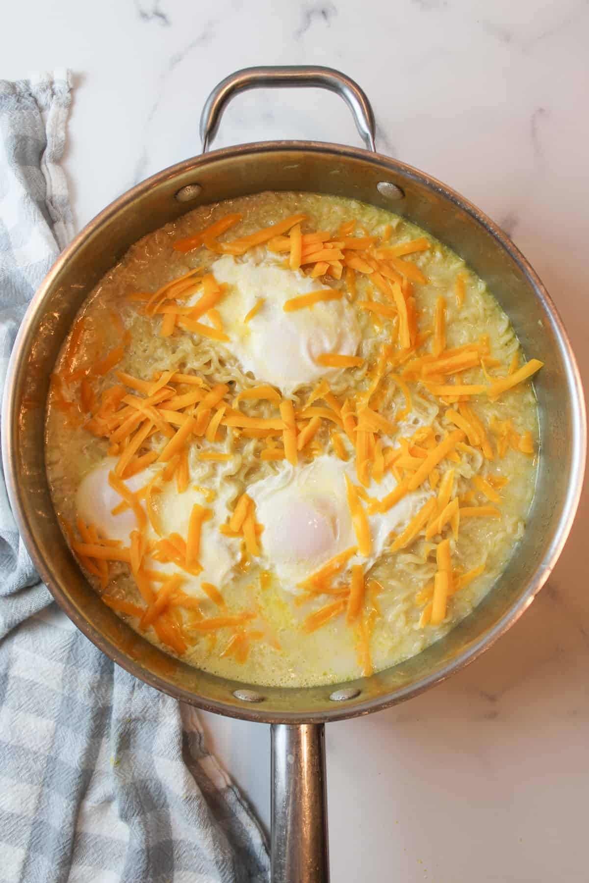 shredded cheese over poached eggs and cooked ramen in a large pan.