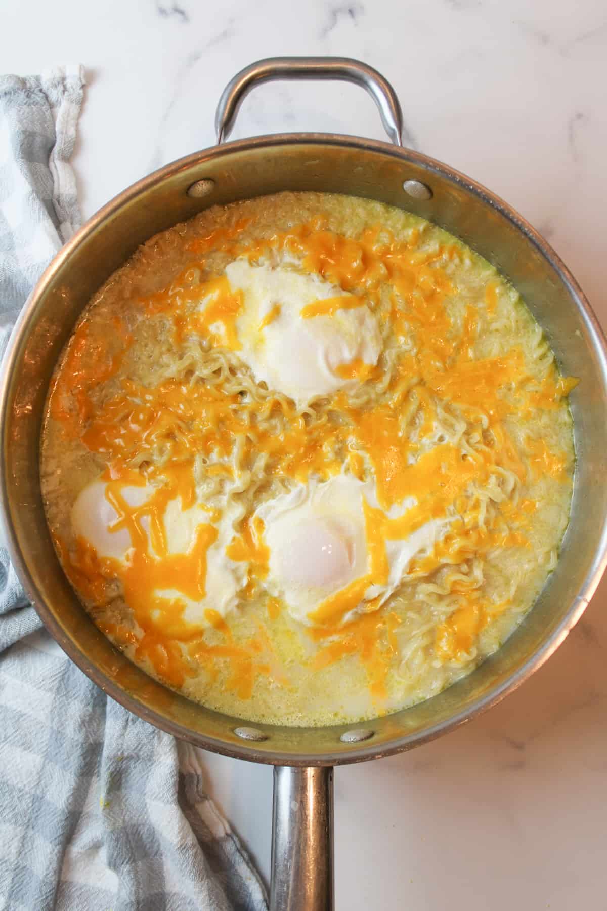 poached eggs on cheesy ramen in a large pan.