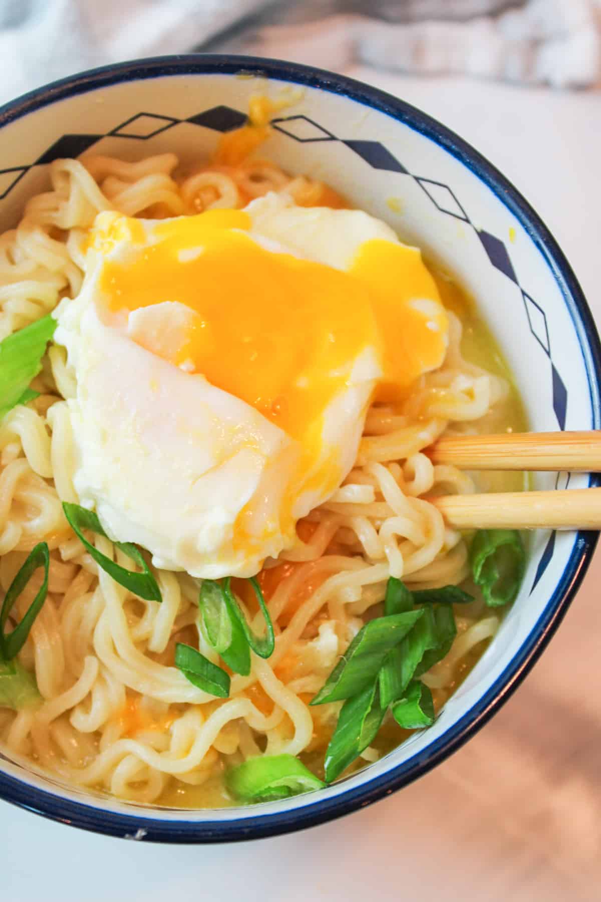 Bowl of cheesy ramen topped with runny yolk egg and green onion slices.