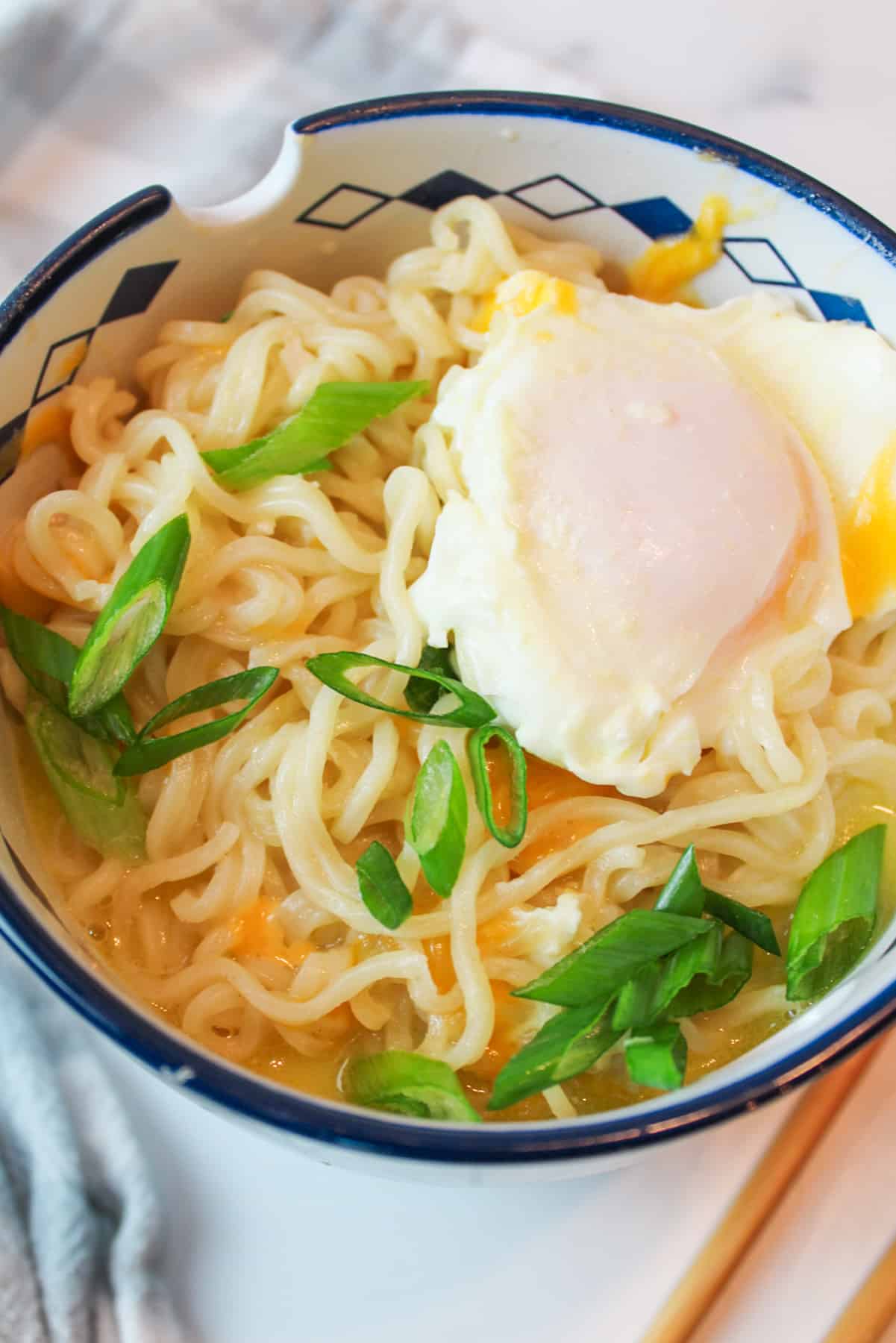 a bowl filled with cheesy ramen, a poached egg, and sliced green onion.