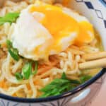 an upclose view of a bowl filled with cheesy ramen and a soft poached egg on top garnished with sliced green onions