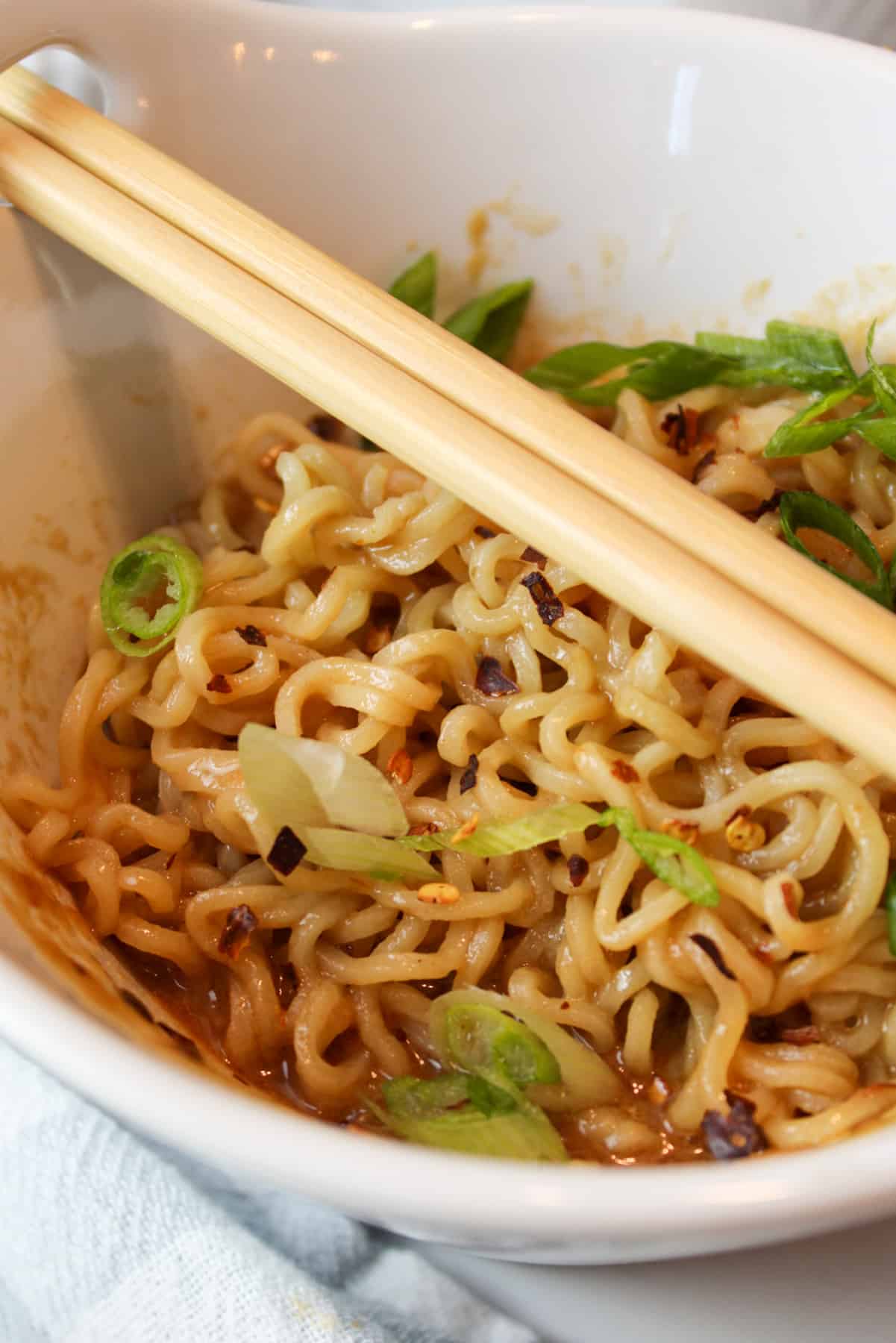 spicy peanut butter ramen in a bowl with sliced green onions and chopsticks.