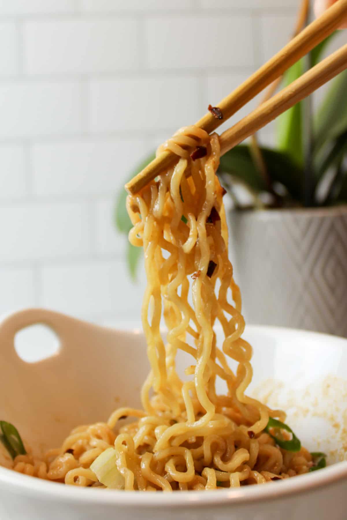 chopsticks holding up a bite of spicy peanut butter ramen.