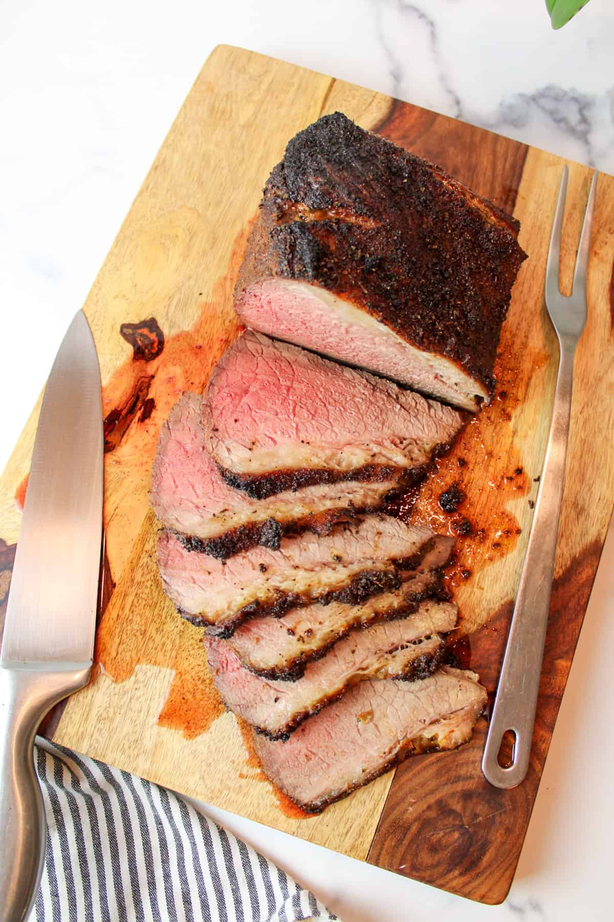 Sliced "poor man's prime rib" on wooden board with carving knife and fork.