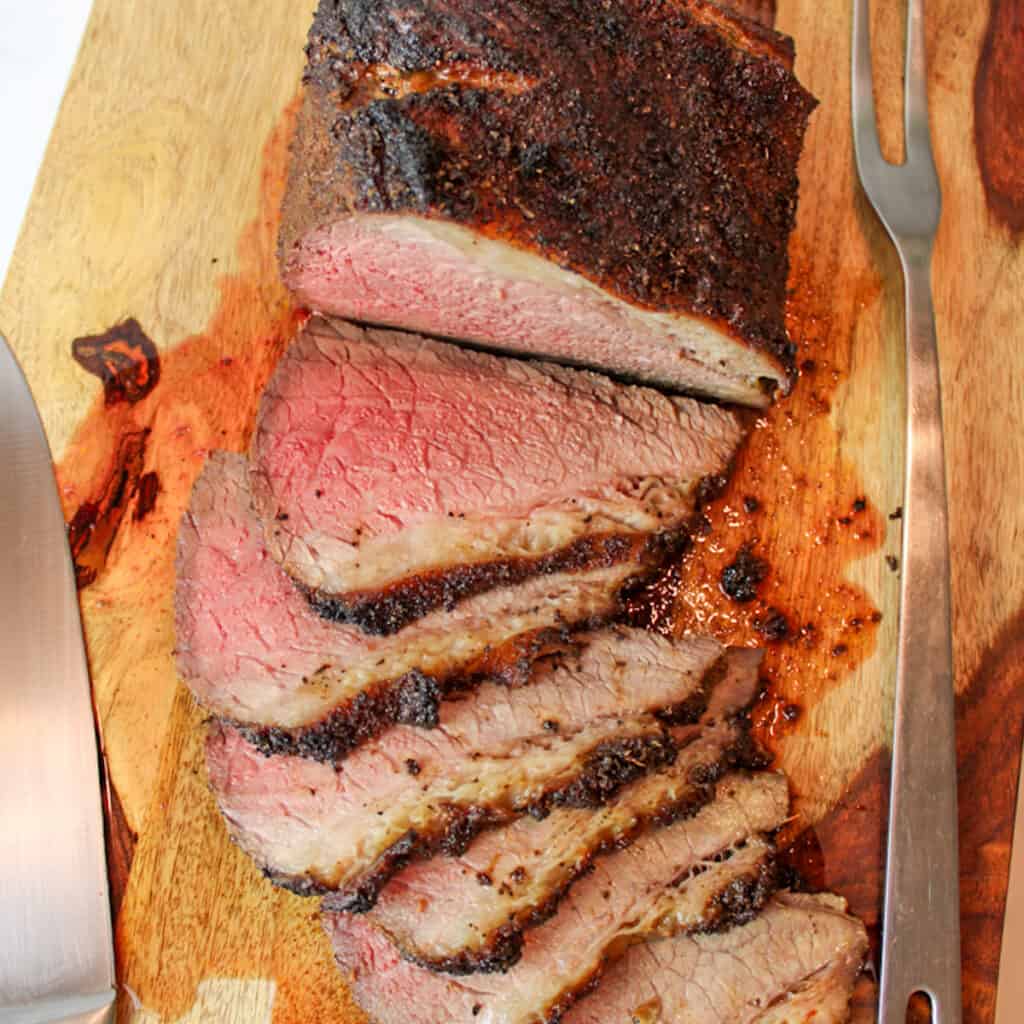a sliced beef roast on a cutting board with carving utensils.