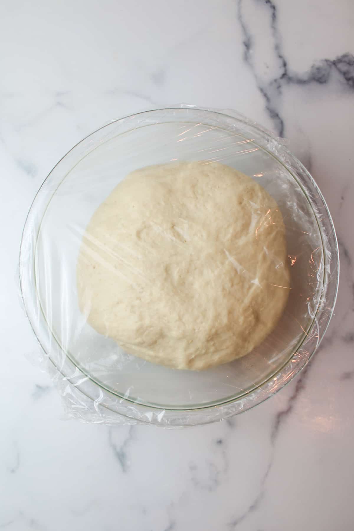 proofed dough in a mixing bowl topped with plastic wrap.