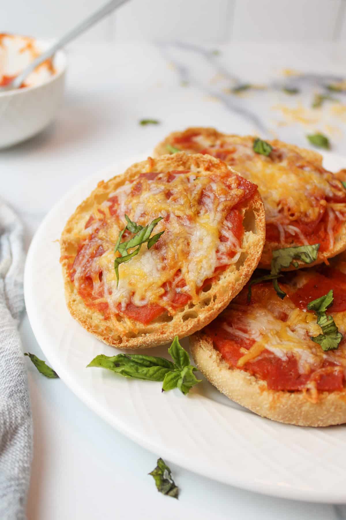 three english muffin pizzas on a white plate with fresh herb garnish